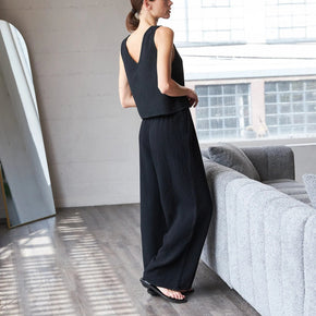 Woman in a black sleeveless top and wide-leg pants standing in a modern living room.