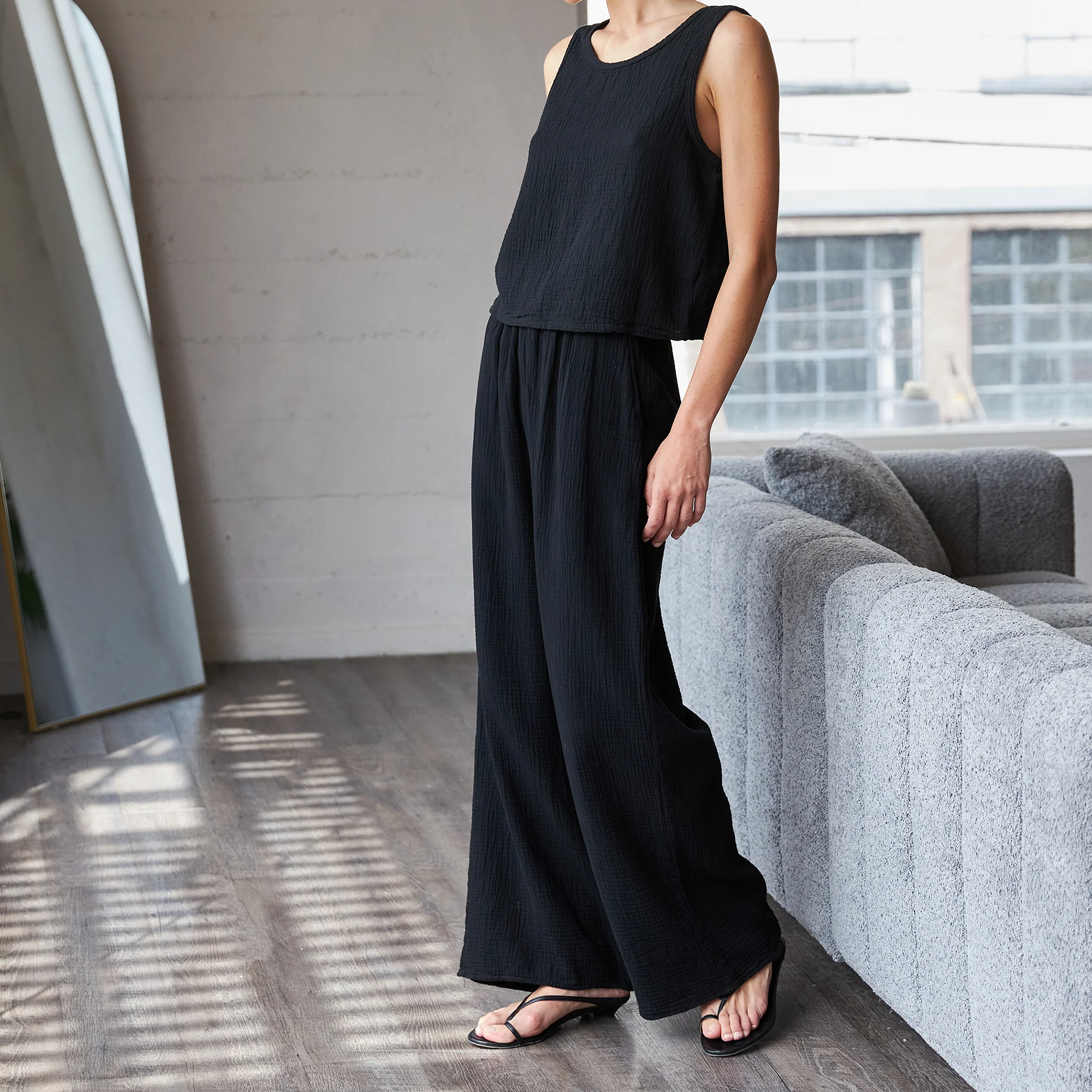 Person wearing a black sleeveless top and wide-leg pants in a modern living room.