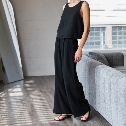 Person wearing a black sleeveless top and wide-leg pants in a modern living room.