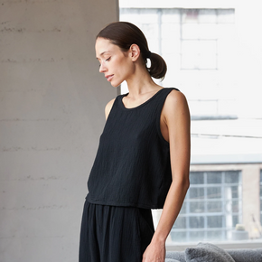 Woman in a black sleeveless top and dark pants standing in a modern living room.
