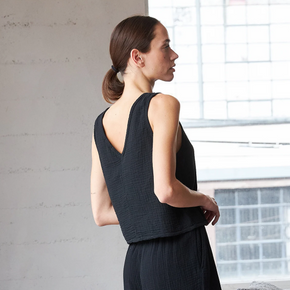 Woman in a black sleeveless top and pants standing in a room with a window and gray sofa.