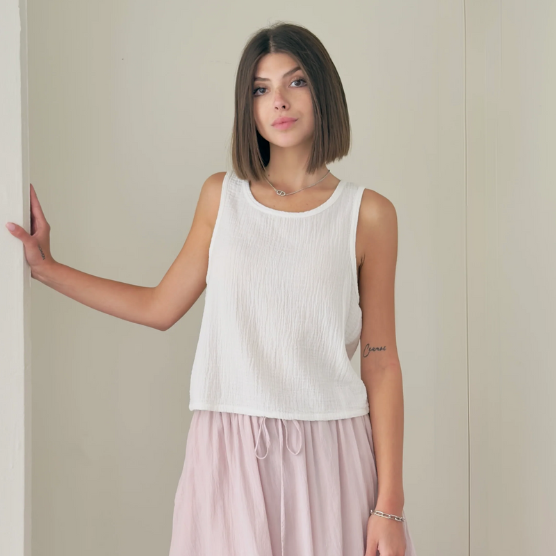 Woman wearing a white sleeveless top and light pink pants against a plain background