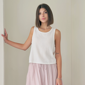 Woman wearing a white sleeveless top and light pink pants against a plain background