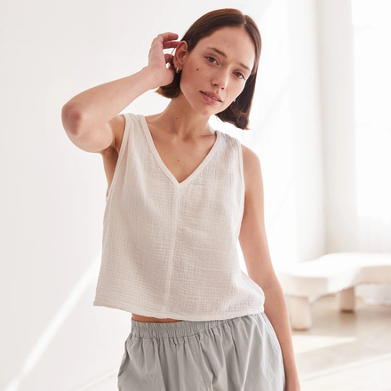 Woman wearing a white sleeveless top and gray pants in a bright room.