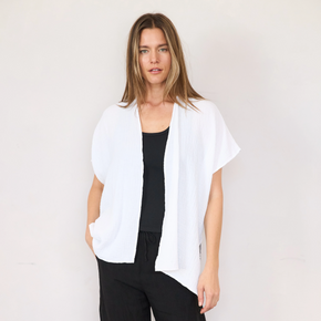 A female model wearing a white, short sleeve, gauze cardigan with an open front, over a black top and black pants.