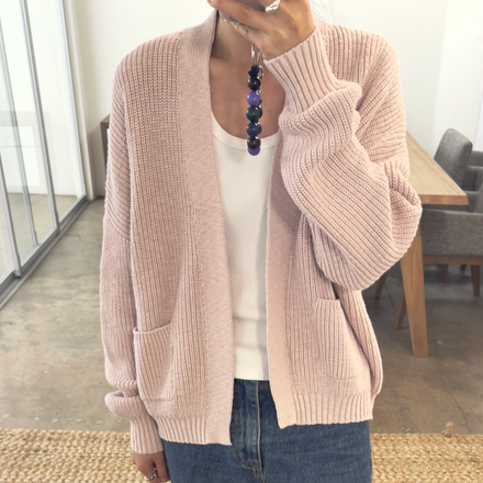 Person wearing a pink cardigan over a white shirt and blue jeans, standing in an indoor setting.