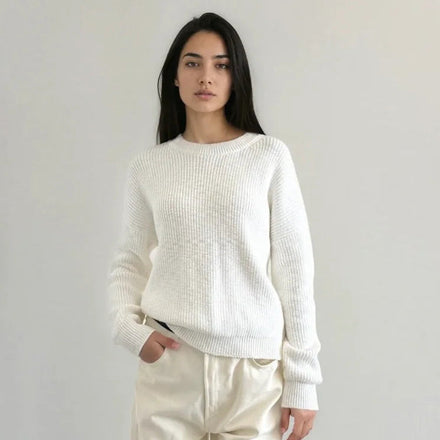 Person wearing a white sweater and beige pants against a plain background