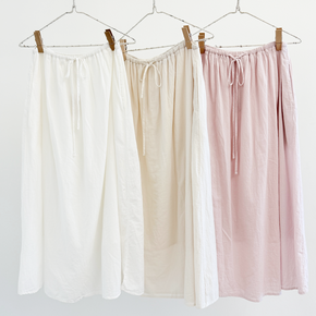 Three pairs of pants in white, beige, and pink hanging on a rack against a white background.