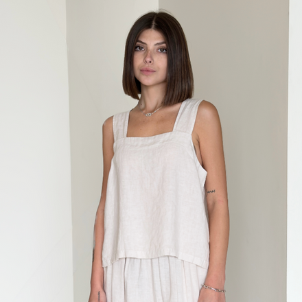 Woman wearing a light-colored sleeveless top and wide-leg pants in a minimalistic setting.
