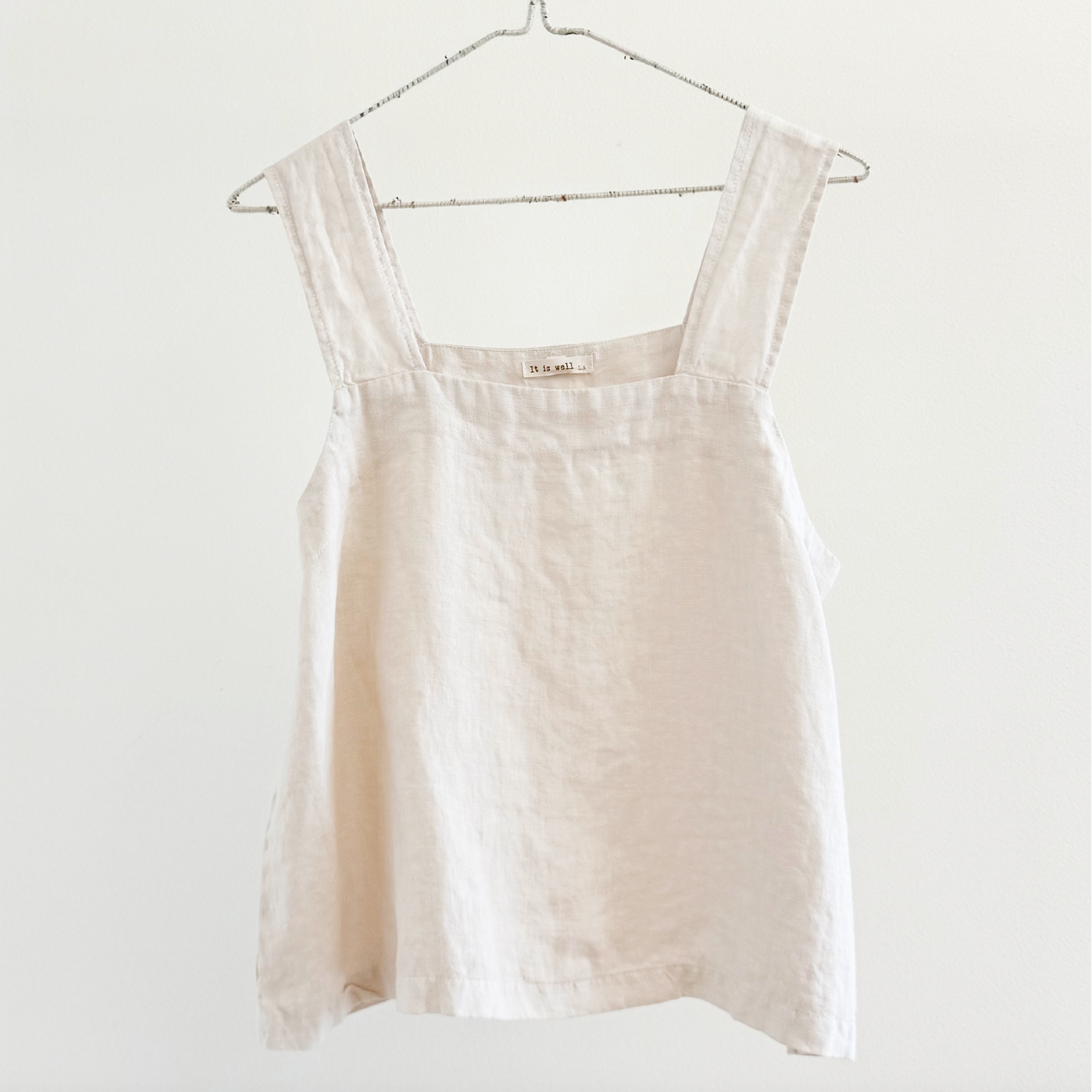 Beige sleeveless top on a hanger against a white background