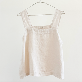 Beige sleeveless top on a hanger against a white background