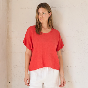 Woman wearing a red top and white shorts against a light beige wall