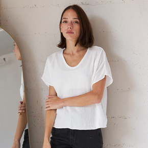 Woman wearing a white t-shirt and black pants standing against a plain wall.