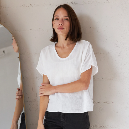 Woman wearing a white t-shirt and black pants standing against a plain wall.