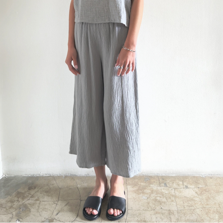 Person wearing a gray sleeveless top and wide-leg pants against a white wall.