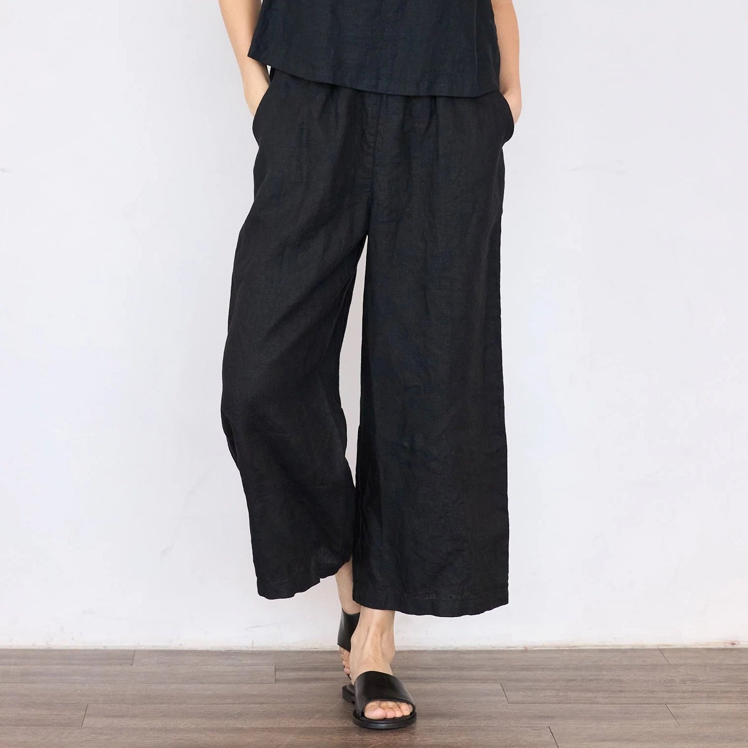 Person wearing a black outfit with wide-leg pants against a white wall.