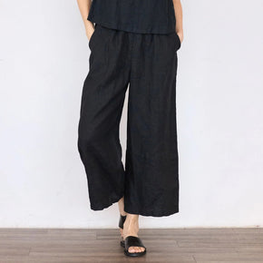 Person wearing a black outfit with wide-leg pants against a white wall.