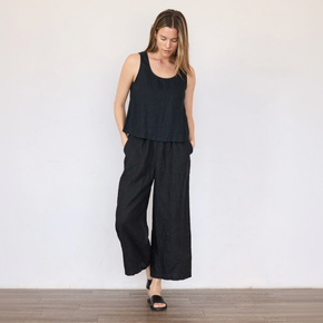 Woman wearing a black sleeveless top and wide-leg pants against a white wall.