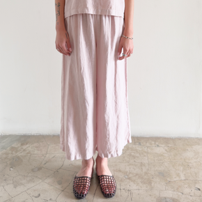 Person wearing a light pink outfit with wide-leg pants and a matching top on a plain background.