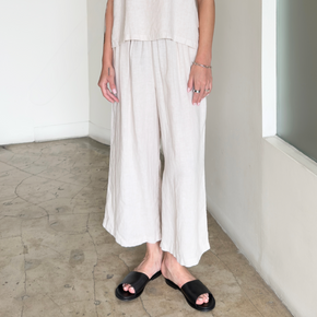 Person wearing white pants and black sandals in a minimal indoor setting