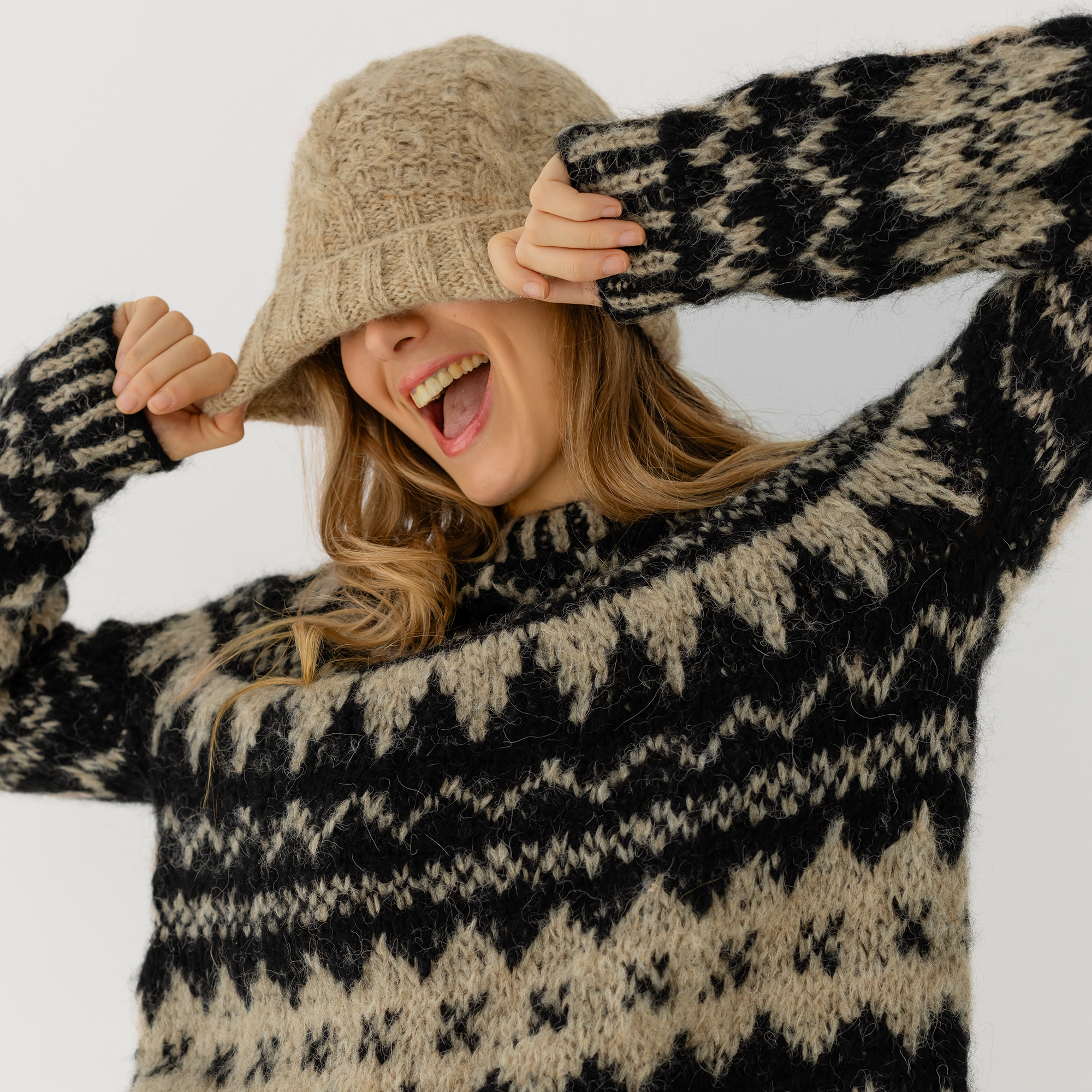 A woman wearing a beige and black patterned knit sweater, posing against a light gray background.