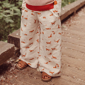 Red Caribou Kids' French Terry Pants - child wearing off white wide-legged pants with elastic waist, pockets and fox print on a wooded background