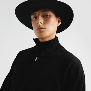 Person wearing a black hat and black sweater against a light gray background