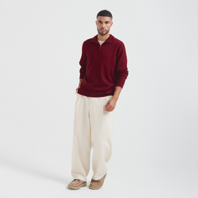 Man wearing a burgundy sweater and white pants on a light gray background
