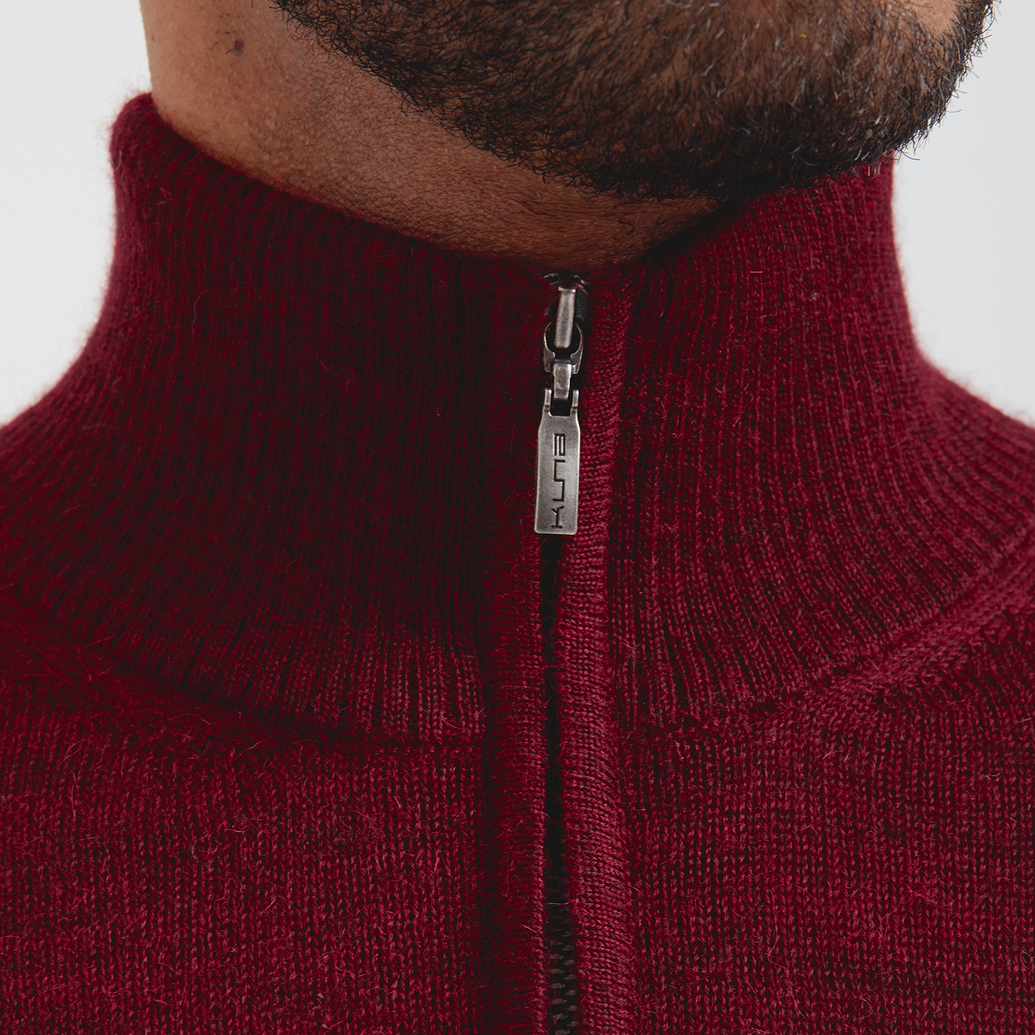 Close-up of a maroon zip-up sweater with a brand logo on a white background