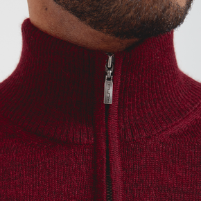 Close-up of a maroon zip-up sweater with a brand logo on a white background
