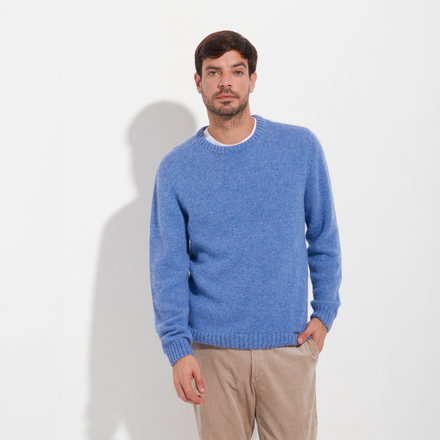 Man wearing a blue sweater and beige pants against a white background
