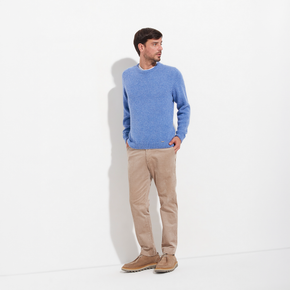 Man wearing a blue sweater and beige pants standing against a white background