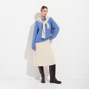 Woman wearing a blue sweater, beige scarf, and skirt with brown boots on a white background