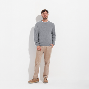 Man wearing a gray sweater and beige pants standing against a white background