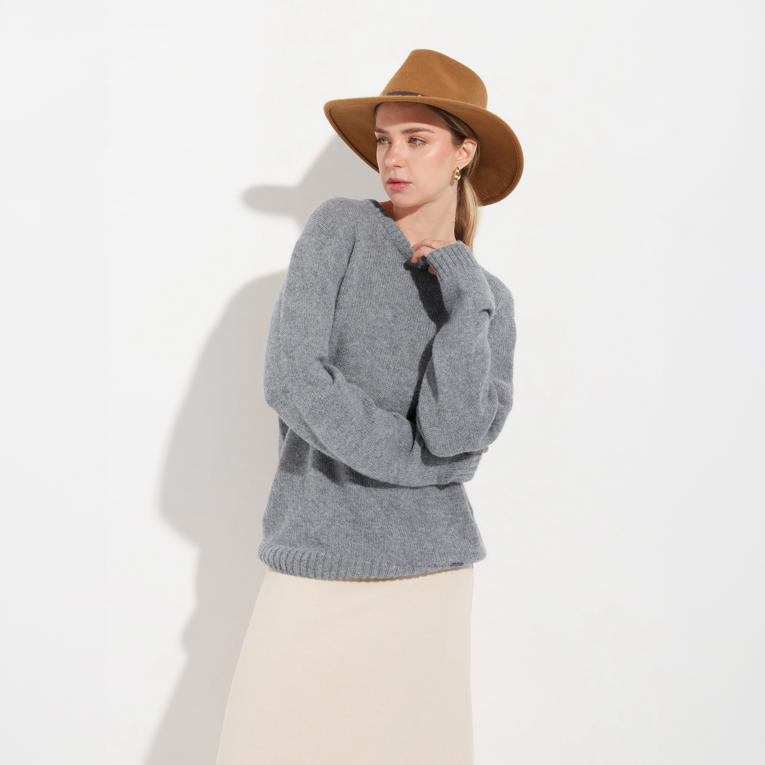 Woman wearing a gray sweater and brown hat against a white background