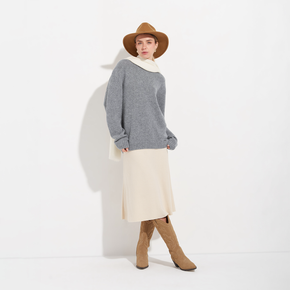 Person wearing a gray sweater, beige skirt, brown boots, and hat on a white background