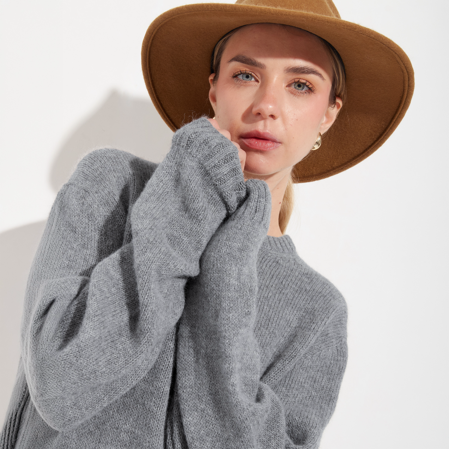 Woman wearing a gray sweater and brown hat on a white background