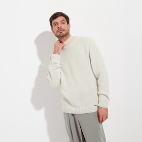 Man wearing a cream sweater and gray pants on a white background