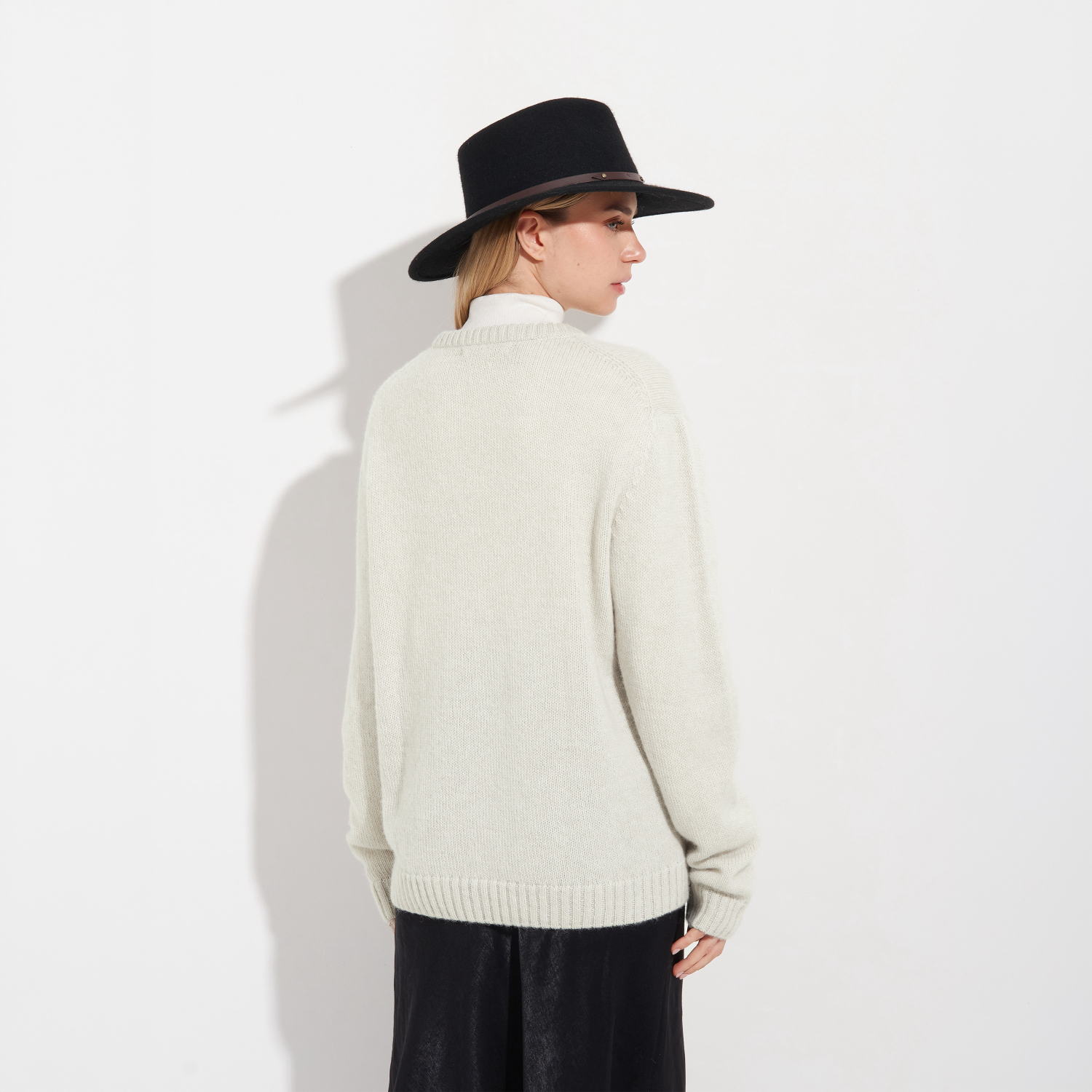 Person wearing a cream sweater and black hat on a white background