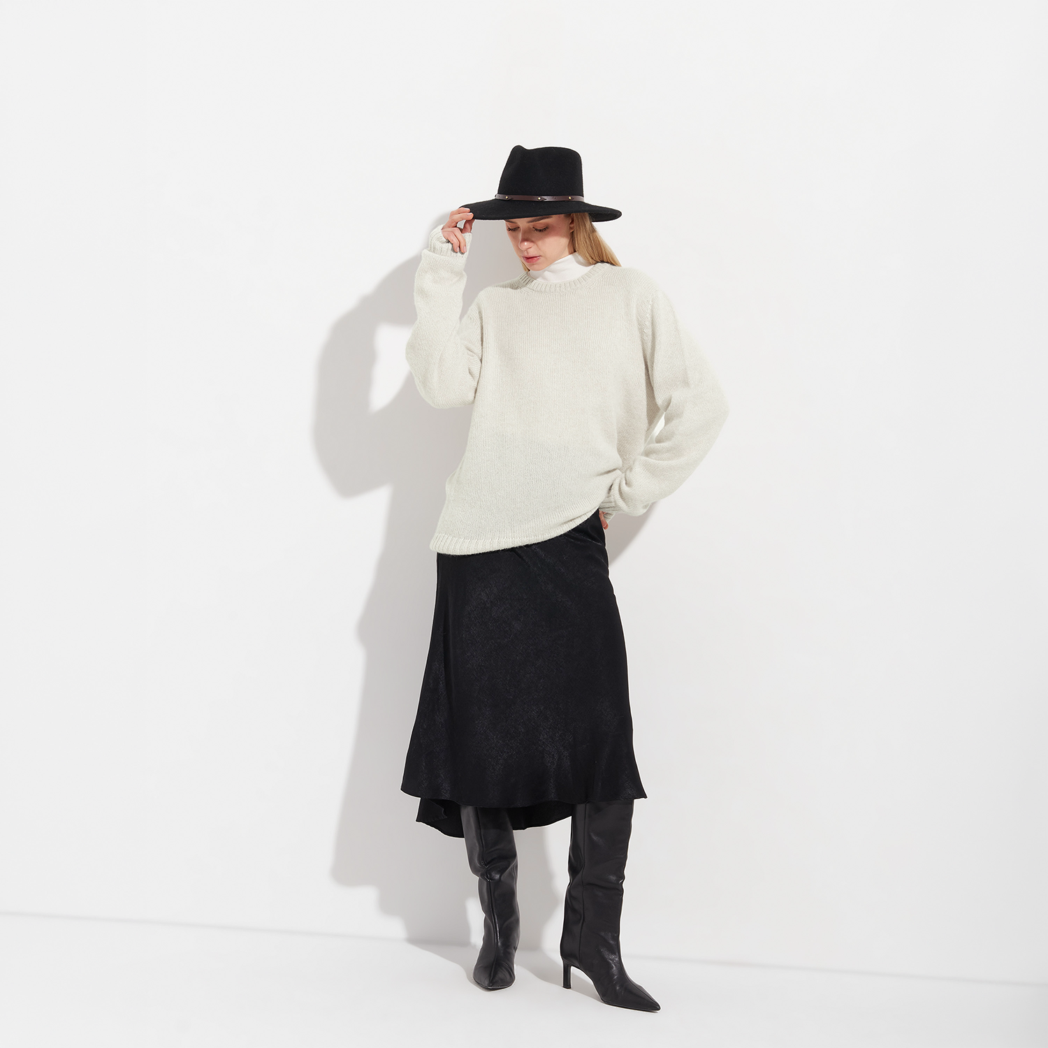 Person wearing a white sweater, black skirt, and black boots on a white background