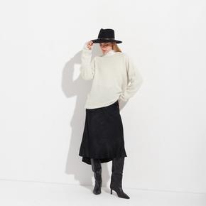Person wearing a white sweater, black skirt, and black boots on a white background