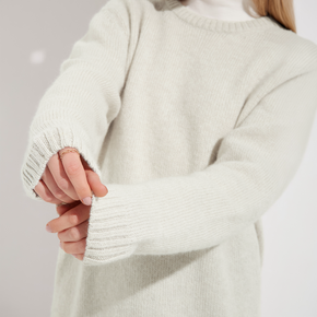 Close-up of a person wearing a light cream sweater with a neutral background