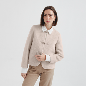 Woman wearing a beige jacket over a white shirt with a plain background