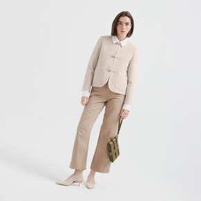 Woman wearing a beige jacket and pants holding a green bag on a white background