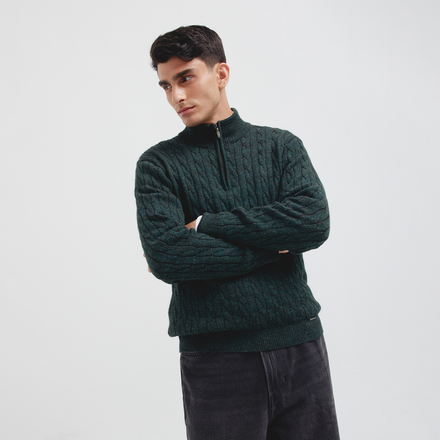 Man wearing a dark green cable knit sweater against a white background