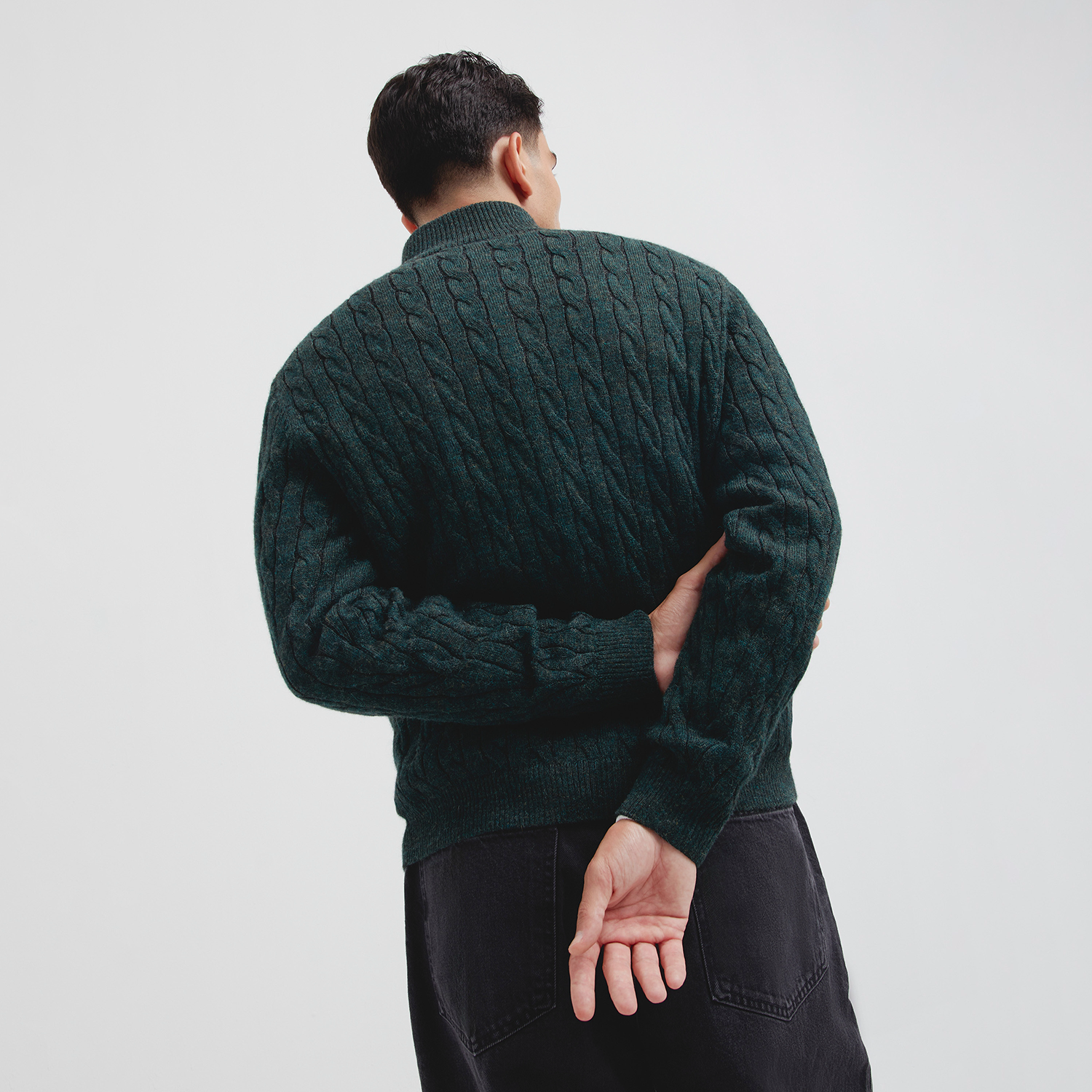 Person wearing a dark green cable knit sweater against a plain background