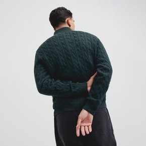 Person wearing a dark green cable knit sweater against a plain background