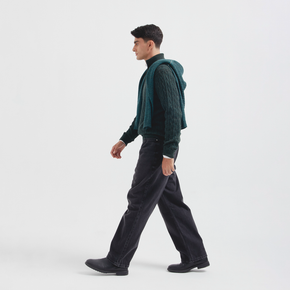 Man wearing a green knitted sweater and black pants on a white background