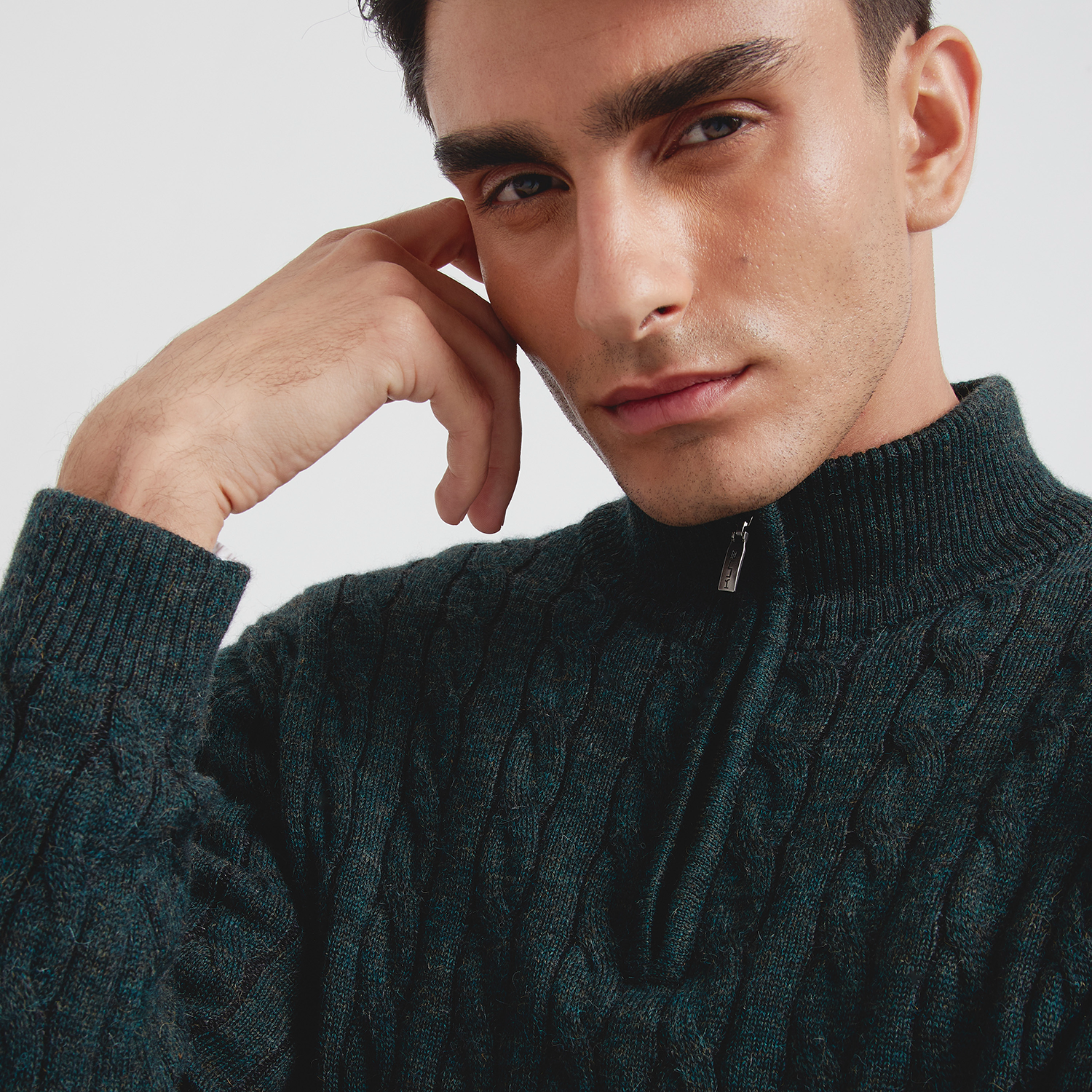 Man wearing a dark green cable knit sweater against a light background