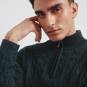 Man wearing a dark green cable knit sweater against a light background